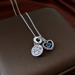 Dettaglio del ciondolo rotondo inciso in argento e del cuore di gemma blu sulla catena