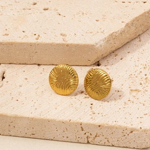 Detail of gold circular stud earrings with water ripple texture on stone background