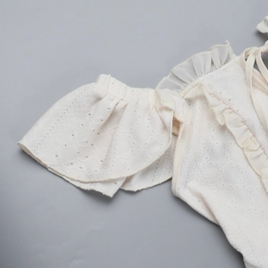 Detailansicht aus weißem Lochspitze-Stoff mit Rüschen und Stickerei auf dem Kleid