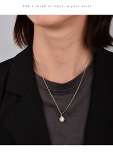 Close-up of a minimalist gold chain necklace with a round white gemstone on a model