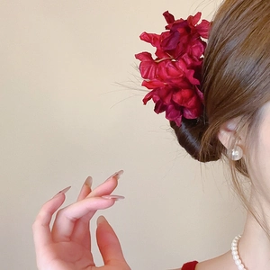 Detail of red fabric flower hairpin showing layered petals and elegant texture in a bun