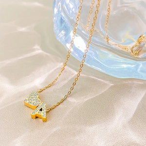Close-up of gold plated necklace with iced out heart and letter A pendant on silk