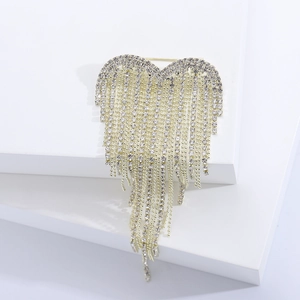 Vue détaillée d'une broche cœur dorée à pompons avec des strass étincelants sur fond blanc