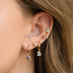 Detail view of gold space-themed earrings with Saturn studs and pink gemstone on the ear