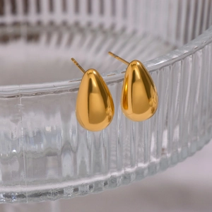Minimalist golden teardrop earrings on a textured glass rim with a soft blur background