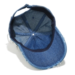 Detailed macro view of denim baseball cap showing distressed edges and metal ring accents