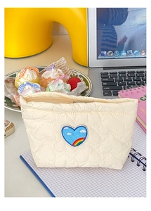 Dettaglio della trousse trapuntata color crema con ricamo a cuore arcobaleno in un set