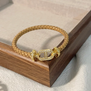Dettaglio di un bracciale in pelle intrecciata cammello con maglia dorata e zirconi su legno