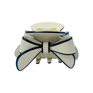 Macro shot of cream-colored resin hair claw with navy blue edges and bow design