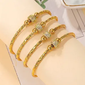 Set of four gold open bangles with sparkling zircon beads and textured metal carvings