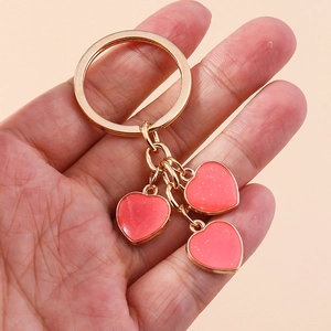 Golden keychain featuring three coral pink heart charms with a subtle glitter finish