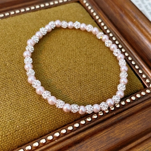 Macro shot of pink pearl bracelet with rhinestone pavé balls on olive green fabric