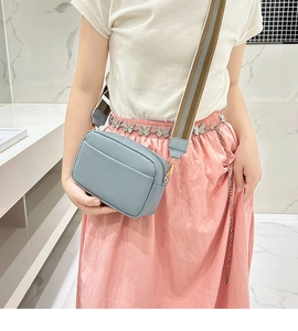 Light blue lychee texture crossbody camera bag with wide striped shoulder strap on model