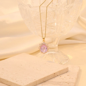 Close-up of gold oval pendant with purple stone and diamonds on a stone surface