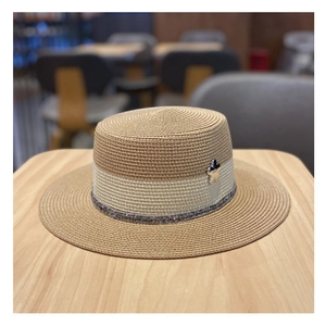 Dettaglio del cappello di paglia estivo con trama intrecciata e ciondolo a fiore in metallo