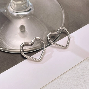 Macro view of silver heart-shaped stainless steel hoop earrings on a glass surface
