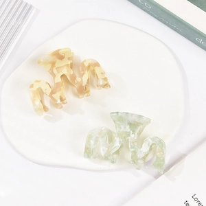 Elegant wavy acetate hair claws in cream marble and green marble on a ceramic tray