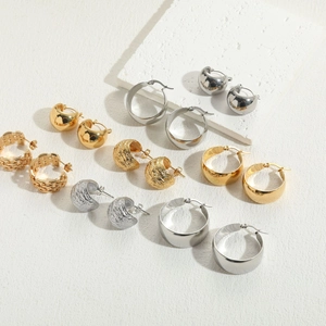 Flat lay of multiple gold and silver titanium steel earrings with various textures on white stone