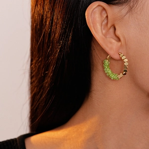 Détail de boucles d'oreilles en C avec billes dorées et éclats de cristal vert