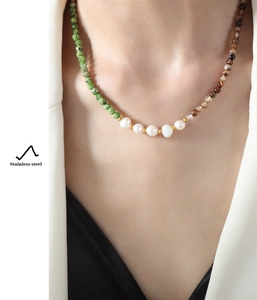 Detail of necklace with baroque pearls, green stones and brown tiger eye on model