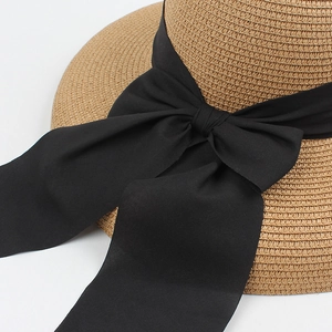 Close-up of hand-woven straw hat texture with elegant black silk ribbon bow detail