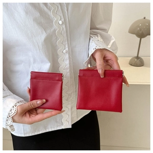 Detail of two red leather squeeze pouches in different sizes held in hand for scale