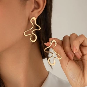 Close-up of oversized gold wavy earrings with abstract irregular lines worn by a model
