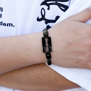Nahaufnahme eines schwarzen geflochtenen Armbands mit Rasierklingen-Anhänger aus Edelstahl