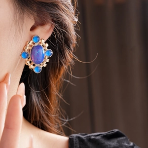 Detail of vintage palace style earring with oval blue stone and golden metal on model