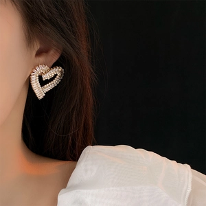 Close-up of elegant gold heart-shaped zircon earrings worn by a model in soft lighting