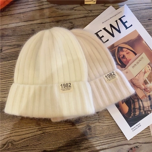 Flat lay of cream knitted beanies with 1982 California embroidery on wooden background