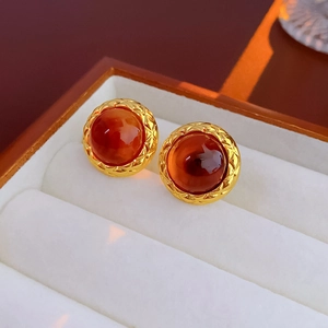 Macro shot of vintage round gold earrings with red gemstone and checkered metal texture