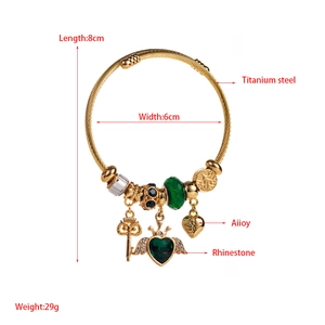 Close-up of gold adjustable charm bracelet with heart pendant and green beads