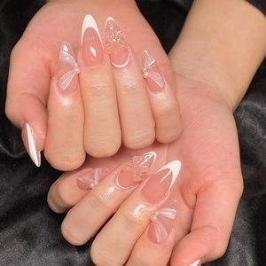 Macro detail of nude French almond press-on nails with 3D bows and pearls on black satin
