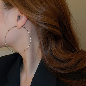Detailed view of large minimalist silver hoop earrings worn on ear with chic outfit