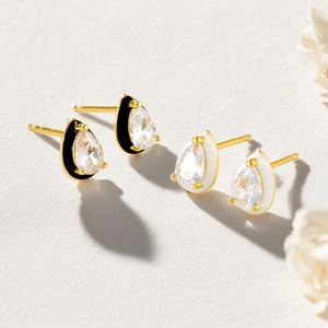 Detail view of pear-shaped gold earrings with clear cubic zirconia and colored enamel borders
