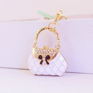 Macro shot of white quilted handbag keychain with gold trim and rhinestone bow accent