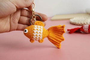 Detailed close-up of a handmade crochet goldfish keychain with orange and white yarn scales