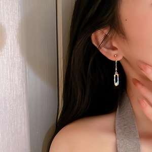 Detail of gold-plated geometric long tassel earrings with crystals worn by a model