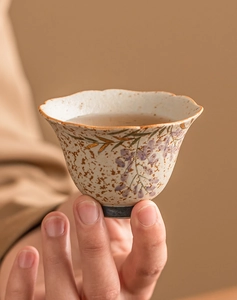 Close-up of hand holding a ceramic teacup with wisteria patterns and gold gilded rim