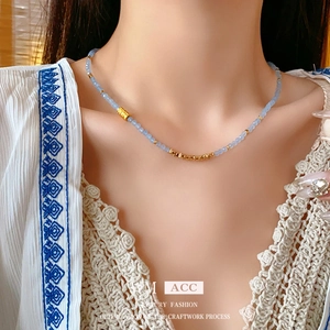 Collier en perles bleues et acier titane avec détails dorés porté sur le cou d'un modèle