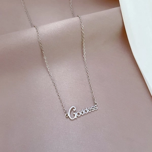 Close-up of a silver Goddess pendant necklace resting on soft pink fabric background