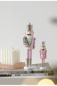 Pink and silver nutcracker soldier figurines on books with warm festive lighting