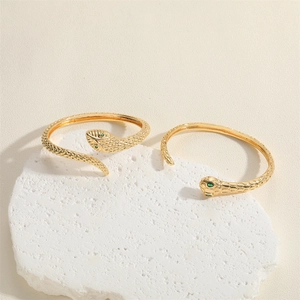 Elegant gold-plated snake wrap bracelet and bangle with green gemstone eyes on stone pedestal