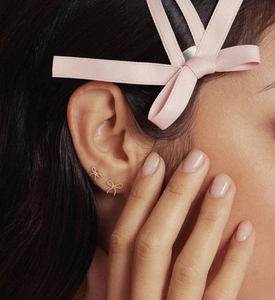 Close-up of golden bow earrings with beaded texture worn by model with pink ribbon