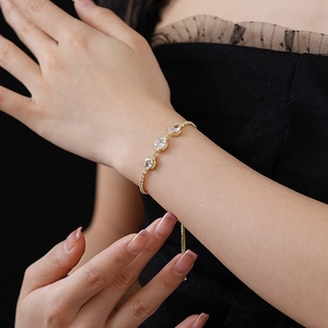 Detail of adjustable gold bracelet featuring oval zircon flower charms on a model wrist