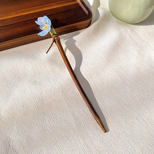 Detail shot of a wooden hair pin with a blue flower and elegant oriental tassel design