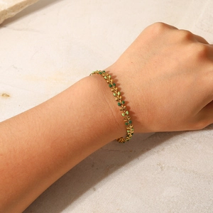 Detail of 18K gold-plated chain bracelet with green enamel leaf charms on a wrist