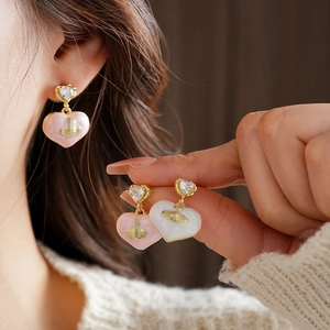 Close-up of heart-shaped gold-plated earrings with pink and white enamel and zircon stones