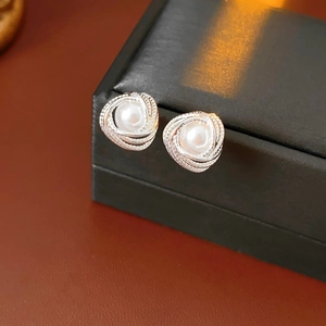 Macro shot of silver spiral earrings featuring a white pearl on a black jewelry box